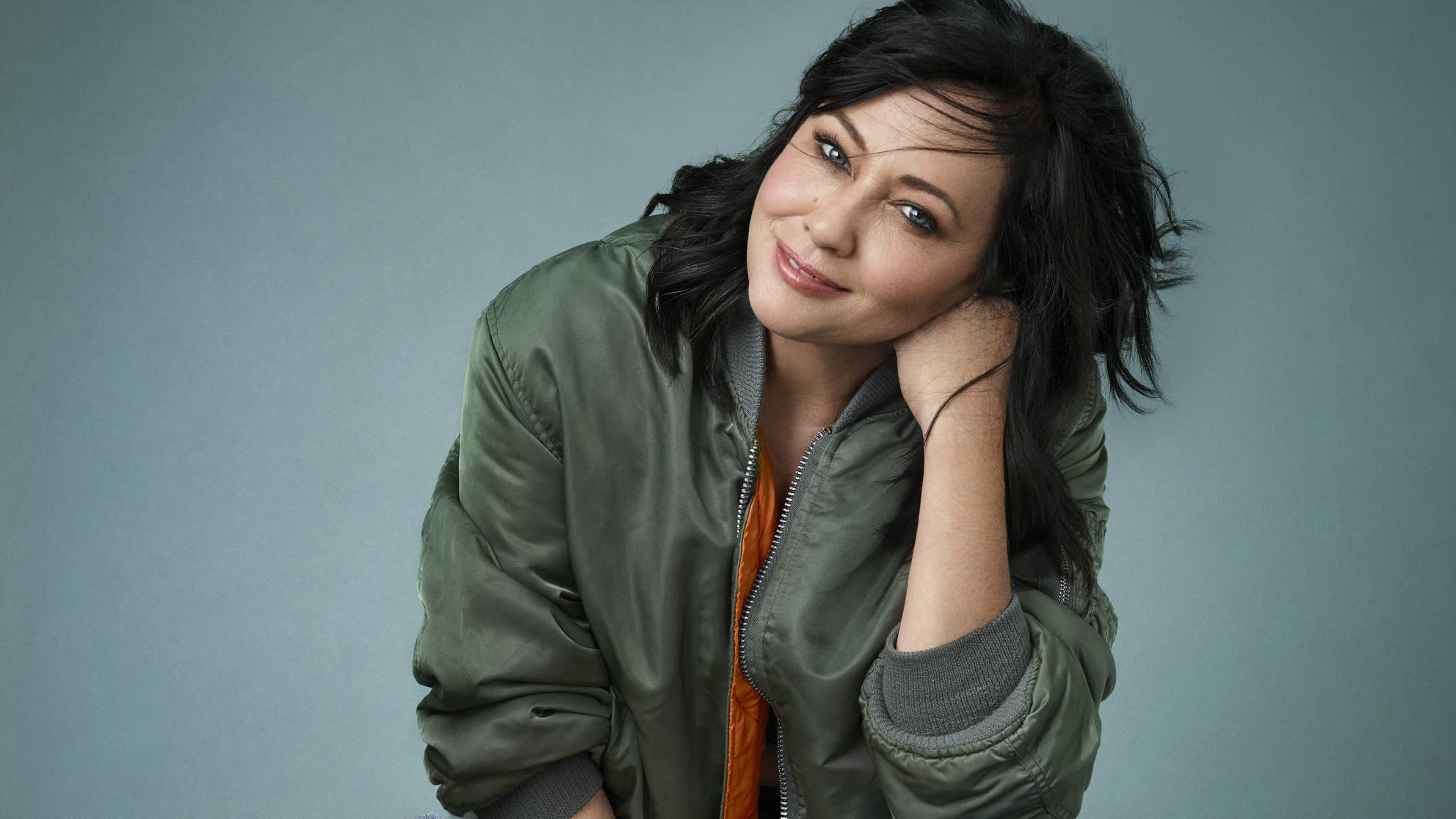 Shannen Doherty wearing an orange shirt and a green jacket