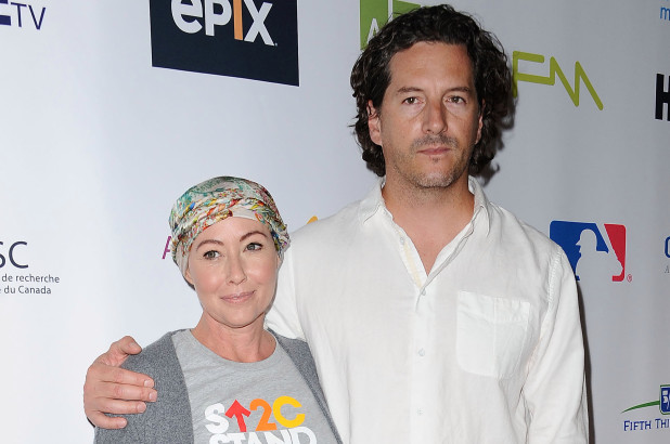 Shannen Doherty and her husband. Doherty is wearing a stand up to cancer t shirt and a head wrap and her husband is wearing a white button down