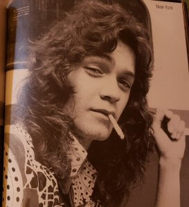 Eddie Van Halen smoking a cigarette at a younger age with long, curly hair