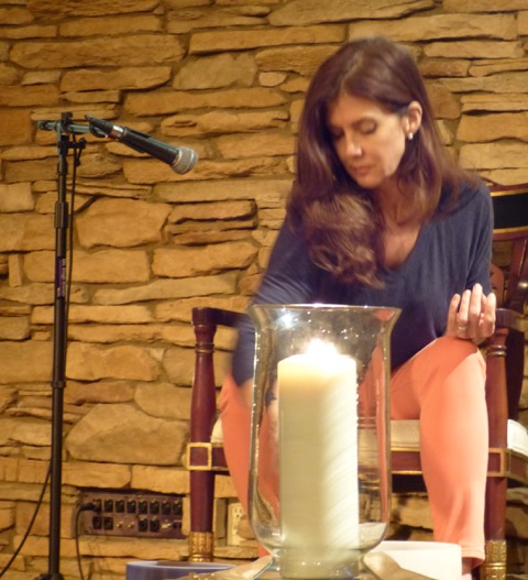 Jean Trebek sitting in a wooden chair in front of a microphone with a candle in front of her leading one of her Religious Science practices