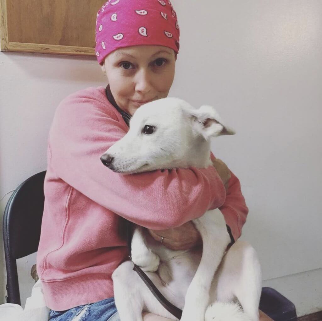 Shannen Doherty with a pink bandana covering her head hugging a dog