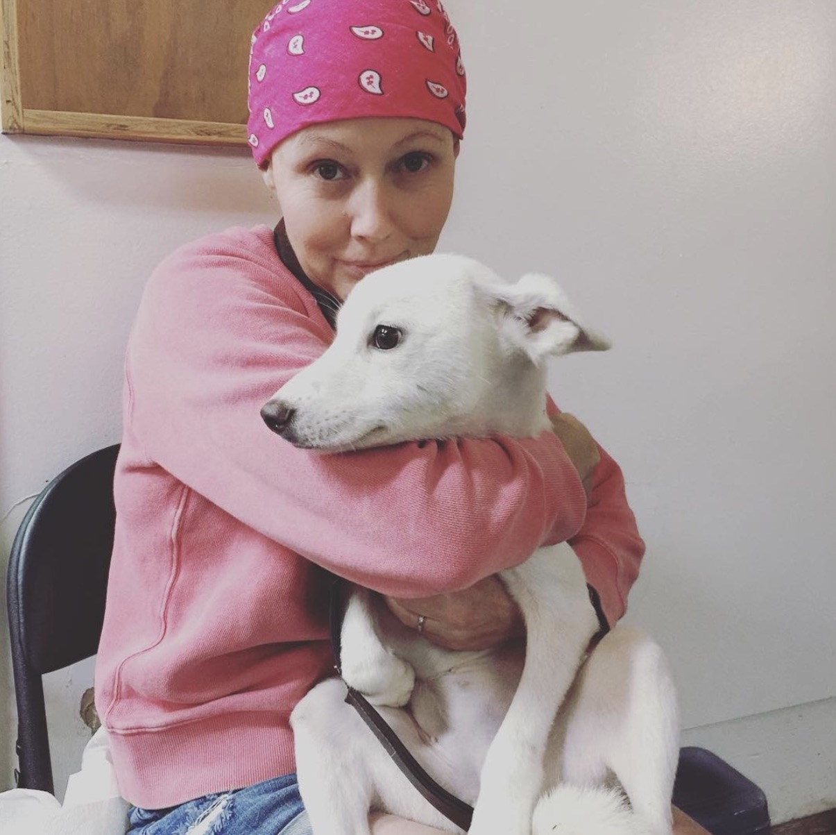 Shannen Doherty with a pink bandana covering her head hugging a dog