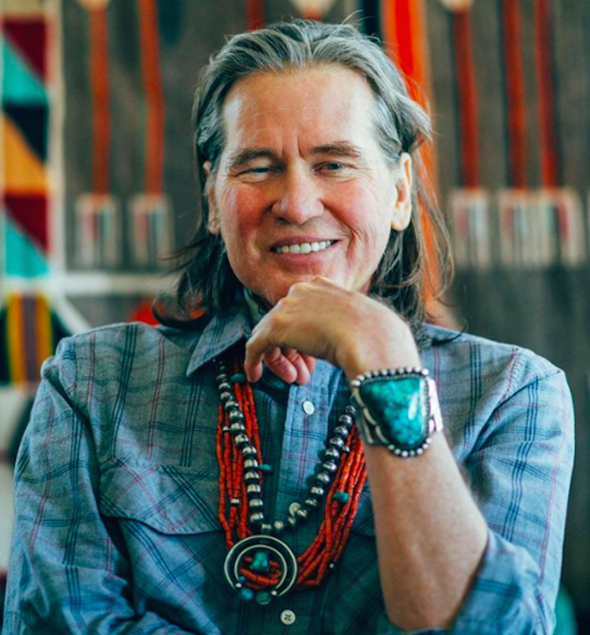 Val Kilmer posing with a blue button down and turquoise jewlery